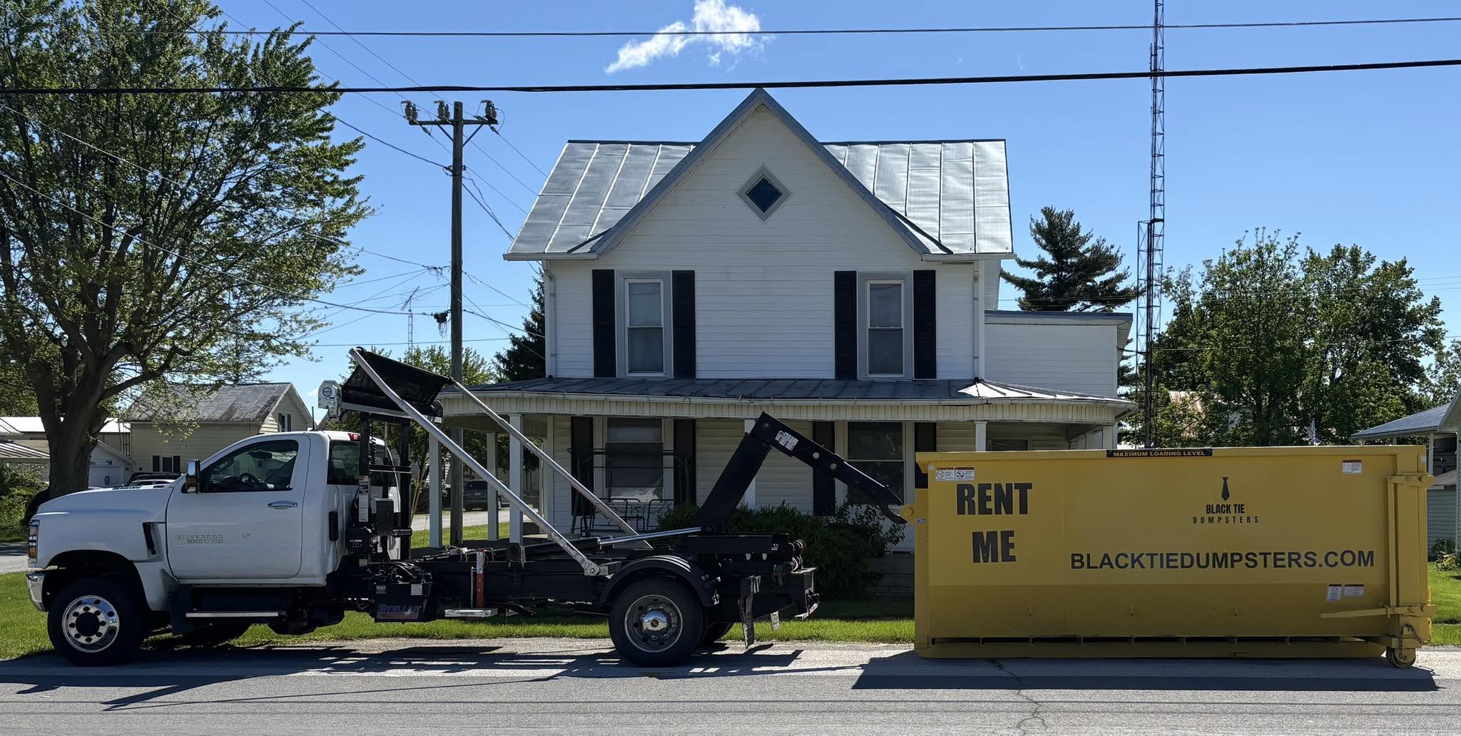 Black Tie Dumpsters roll-off truck delivering a yellow dumpster to a home